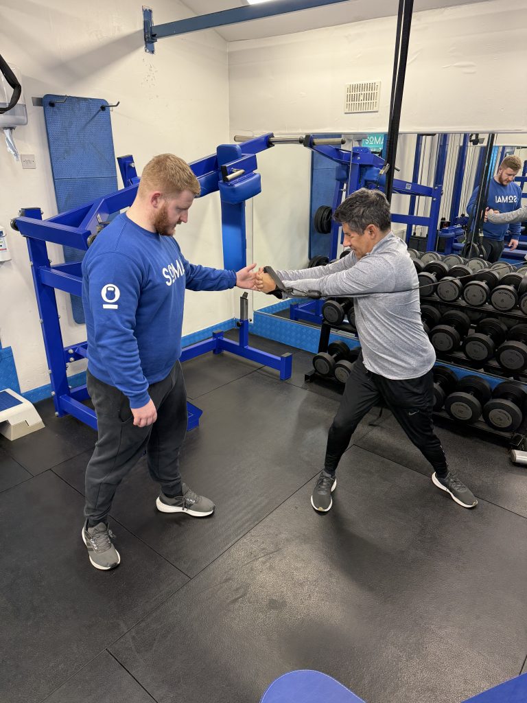 Strength Training for Tennis Players in Altrincham | Soma Fitness Personal trainer coaching a client through a rotational strength exercise at Soma Fitness in Altrincham